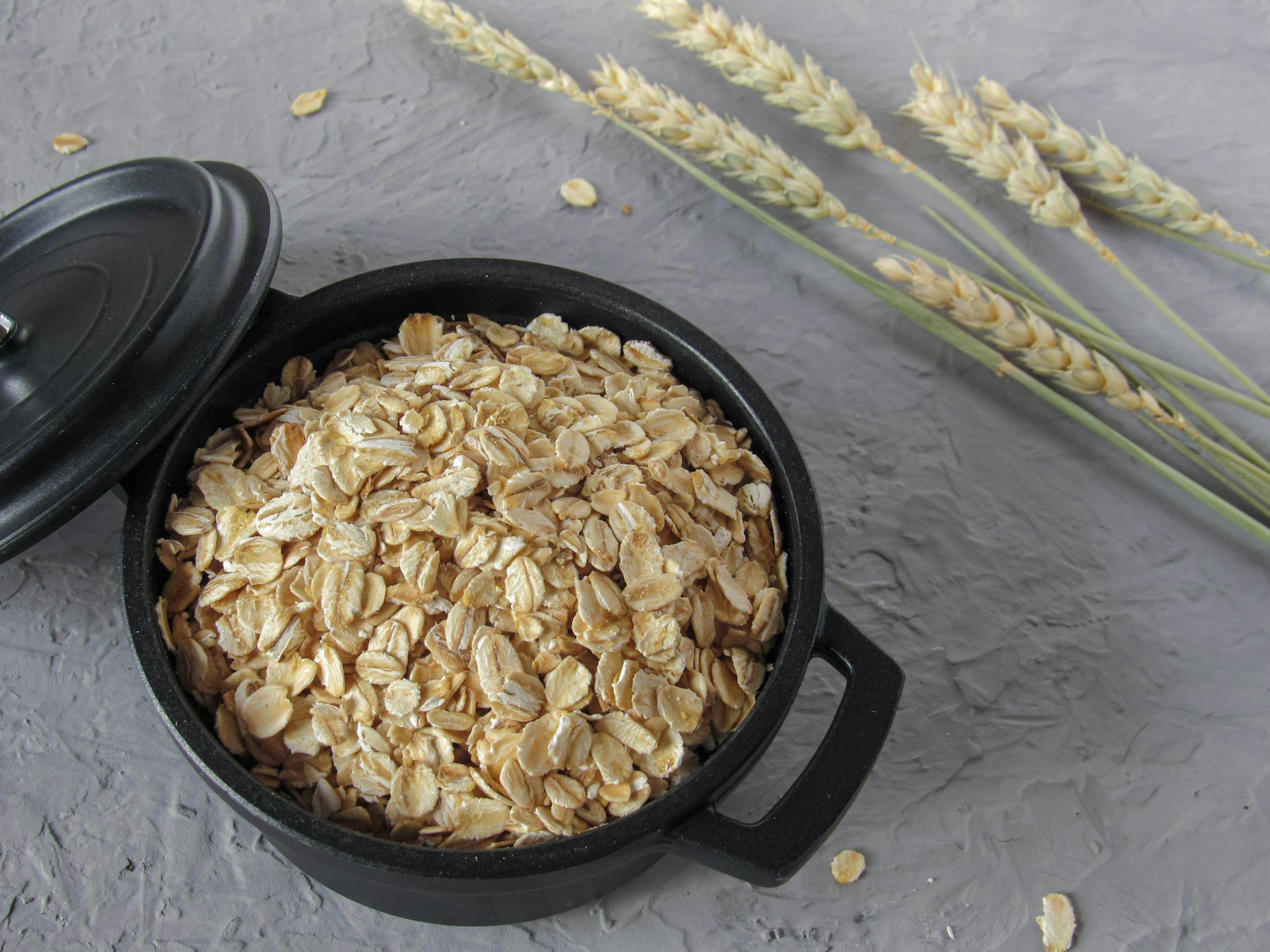 A top-down view of rolled oats in a black pot with wheat stalks, showcasing healthy ingredients.